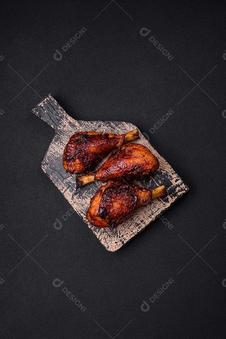Deliciosas pernas de frango grelhado com especiarias e ervas em molho teriyaki sobre um fundo escuro de concreto