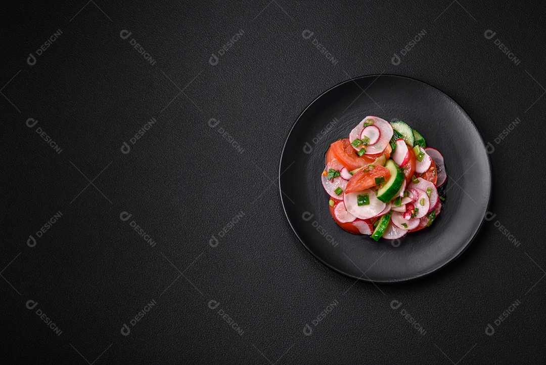 Deliciosa salada vegana de legumes frescos de tomate, pepino e rabanete com sal e especiarias sobre um fundo escuro de concreto