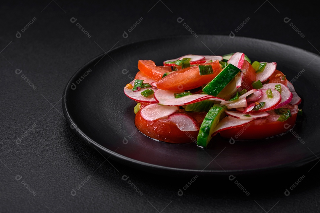 Deliciosa salada vegana de legumes frescos de tomate, pepino e rabanete com sal e especiarias sobre um fundo escuro de concreto