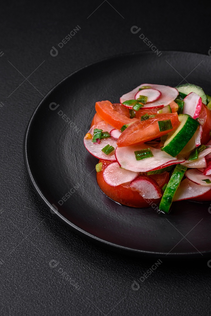 Deliciosa salada vegana de legumes frescos de tomate, pepino e rabanete com sal e especiarias sobre um fundo escuro de concreto