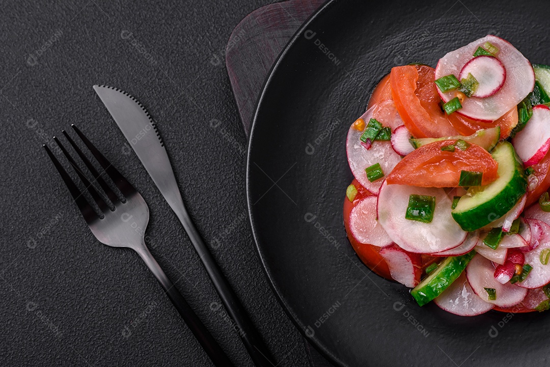 Deliciosa salada vegana de legumes frescos de tomate, pepino e rabanete com sal e especiarias sobre um fundo escuro de concreto