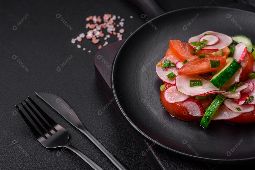Deliciosa salada vegana de legumes frescos de tomate, pepino e rabanete com sal e especiarias sobre um fundo escuro de concreto