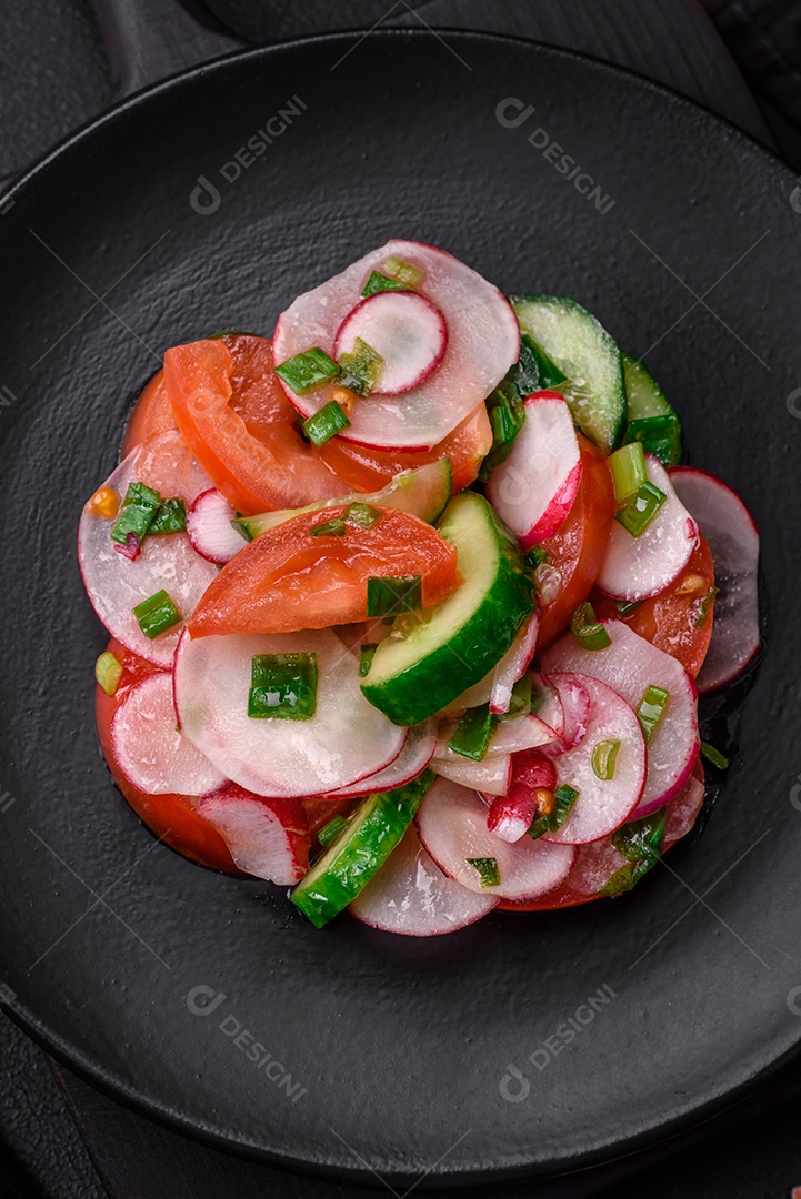 Deliciosa salada vegana de legumes frescos de tomate, pepino e rabanete com sal e especiarias sobre um fundo escuro de concreto
