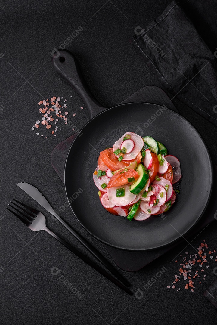 Deliciosa salada vegana de legumes frescos de tomate, pepino e rabanete com sal e especiarias sobre um fundo escuro de concreto