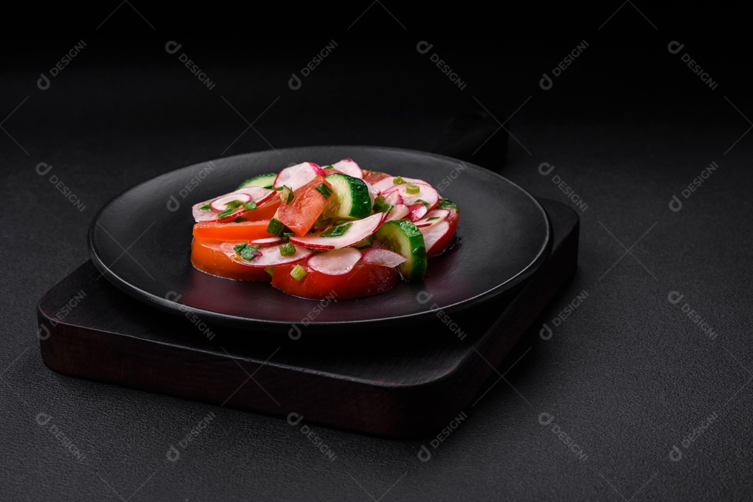 Deliciosa salada vegana de legumes frescos de tomate, pepino e rabanete com sal e especiarias sobre um fundo escuro de concreto