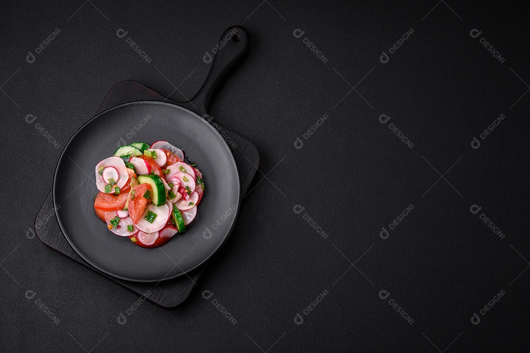 Deliciosa salada vegana de legumes frescos de tomate, pepino e rabanete com sal e especiarias sobre um fundo escuro de concreto