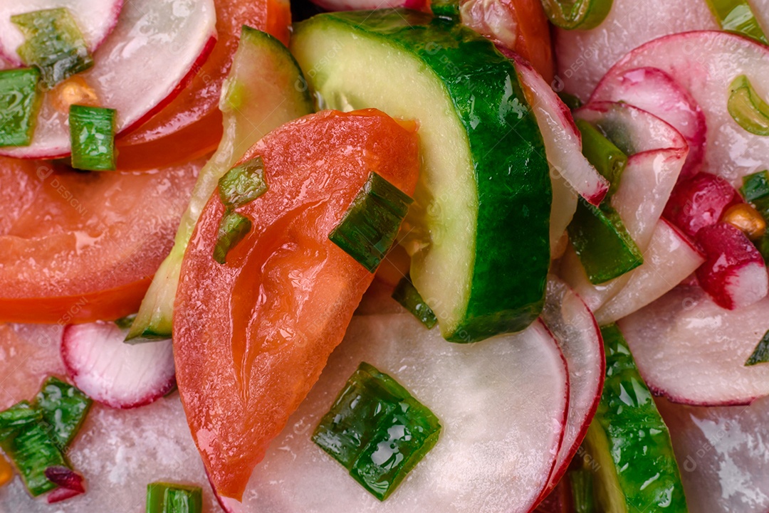 Deliciosa salada vegana de legumes frescos de tomate, pepino e rabanete com sal e especiarias sobre um fundo escuro de concreto