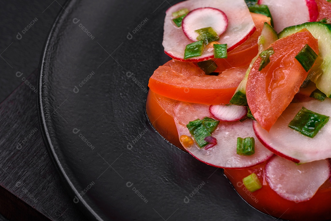 Deliciosa salada vegana de legumes frescos de tomate, pepino e rabanete com sal e especiarias sobre um fundo escuro de concreto