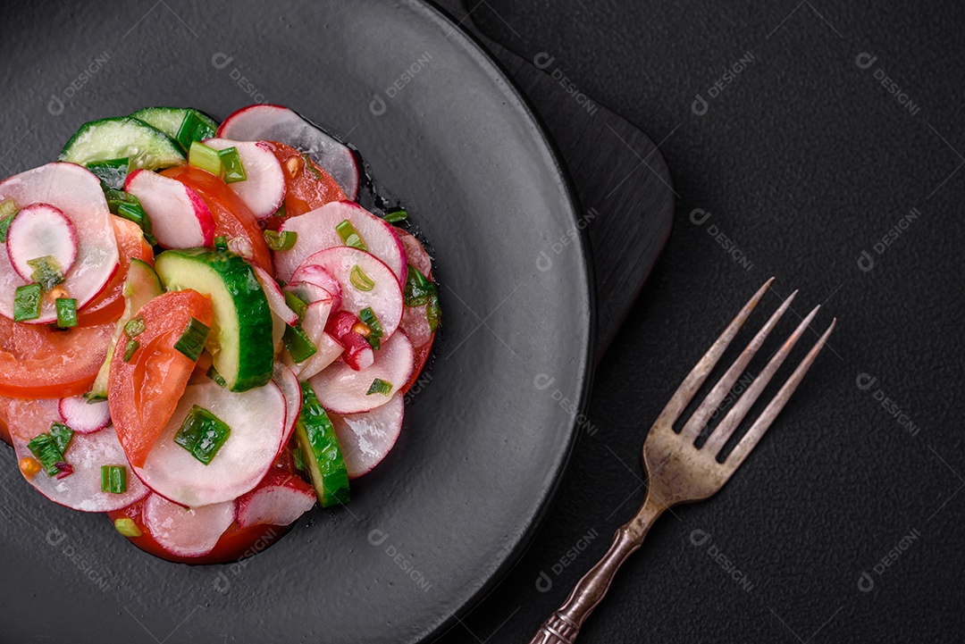 Deliciosa salada vegana de legumes frescos de tomate, pepino e rabanete com sal e especiarias sobre um fundo escuro de concreto