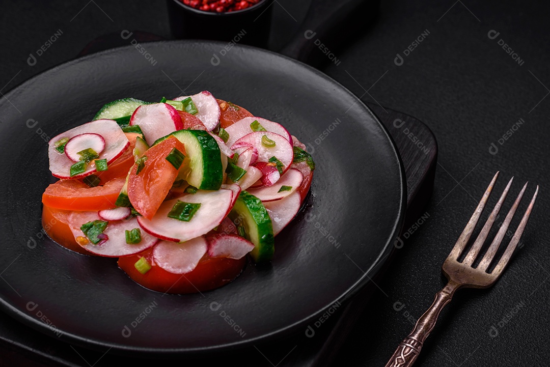 Deliciosa salada vegana de legumes frescos de tomate, pepino e rabanete com sal e especiarias sobre um fundo escuro de concreto