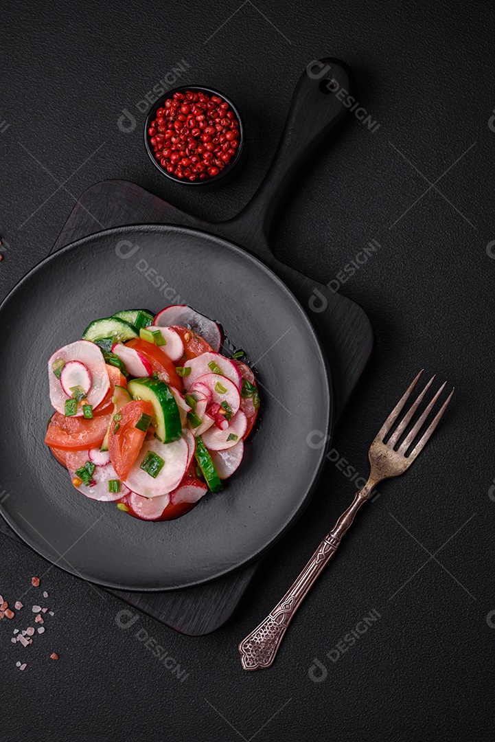 Deliciosa salada vegana de legumes frescos de tomate, pepino e rabanete com sal e especiarias sobre um fundo escuro de concreto