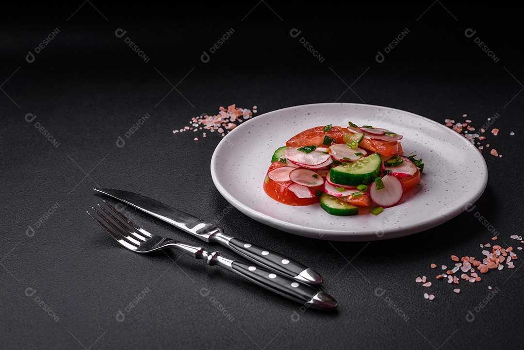 Deliciosa salada vegana de legumes frescos de tomate, pepino e rabanete com sal e especiarias sobre um fundo escuro de concreto