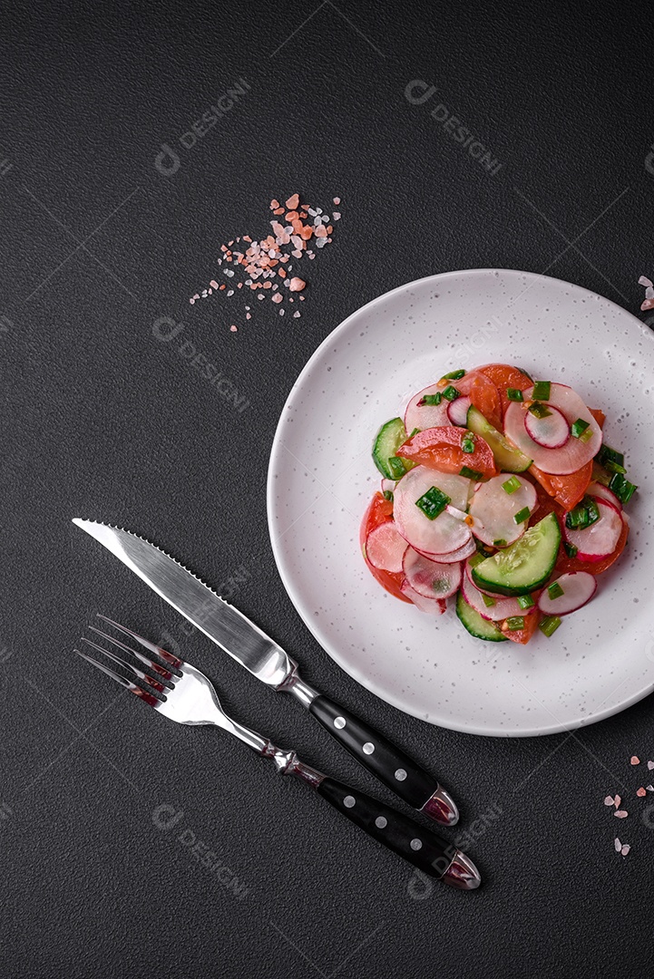 Deliciosa salada vegana de legumes frescos de tomate, pepino e rabanete com sal e especiarias sobre um fundo escuro de concreto