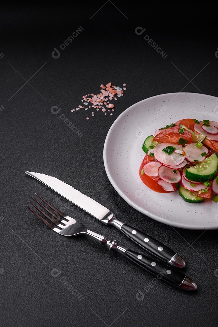 Deliciosa salada vegana de legumes frescos de tomate, pepino e rabanete com sal e especiarias sobre um fundo escuro de concreto