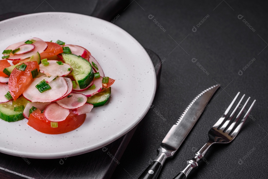 Deliciosa salada vegana de legumes frescos de tomate, pepino e rabanete com sal e especiarias sobre um fundo escuro de concreto