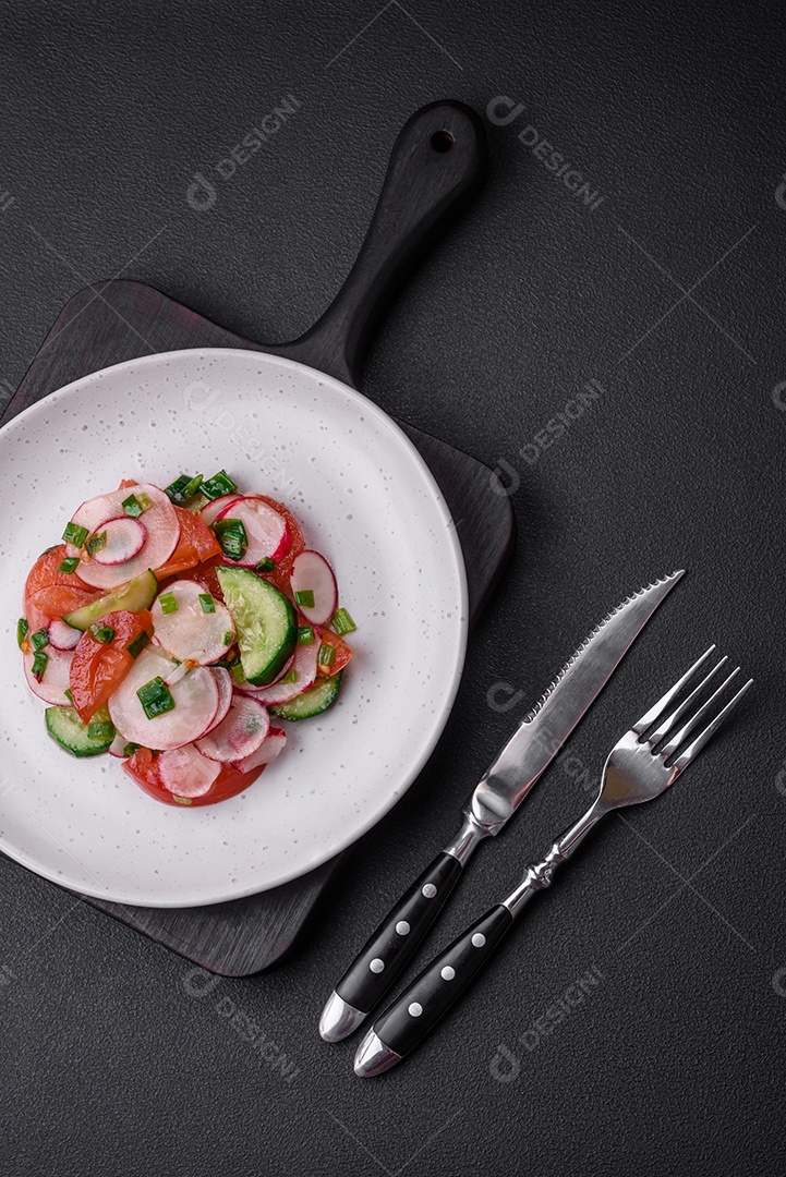 Deliciosa salada vegana de legumes frescos de tomate, pepino e rabanete com sal e especiarias sobre um fundo escuro de concreto