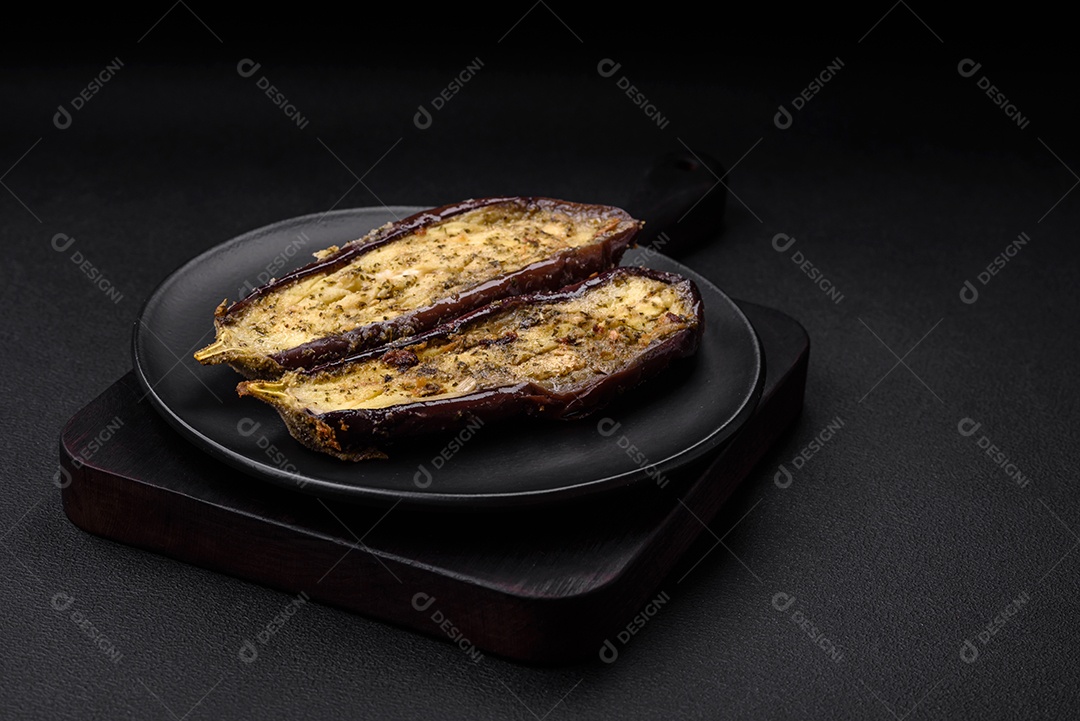Deliciosa berinjela cortada em duas metades assada com sal, especiarias e ervas sobre um fundo escuro de concreto