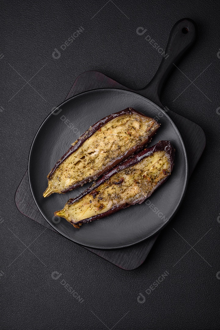 Deliciosa berinjela cortada em duas metades assada com sal, especiarias e ervas sobre um fundo escuro de concreto