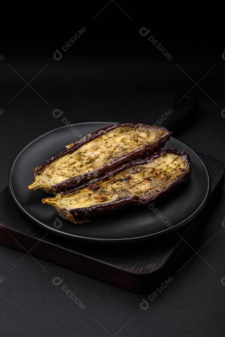 Deliciosa berinjela cortada em duas metades assada com sal, especiarias e ervas sobre um fundo escuro de concreto