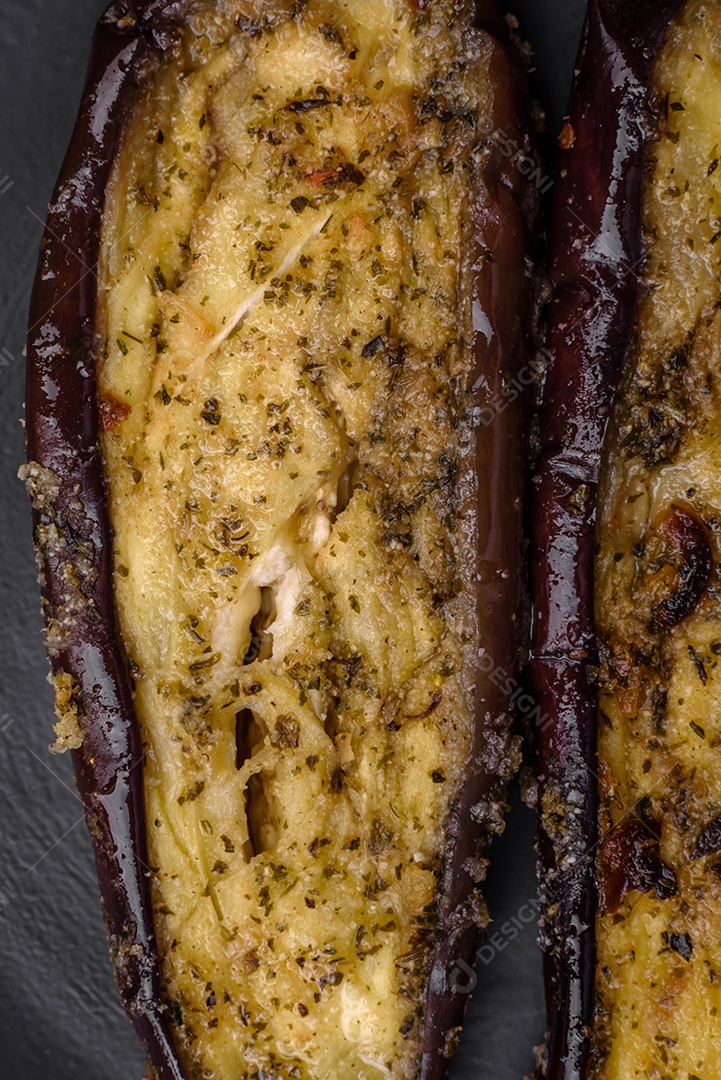 Deliciosa berinjela cortada em duas metades assada com sal, especiarias e ervas sobre um fundo escuro de concreto