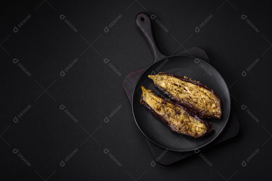 Deliciosa berinjela cortada em duas metades assada com sal, especiarias e ervas sobre um fundo escuro de concreto