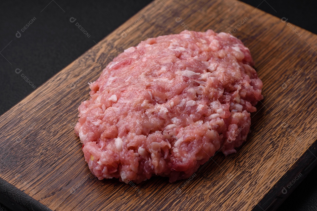 Carne picada crua, carne de porco ou frango com sal, especiarias e ervas sobre um fundo escuro de concreto