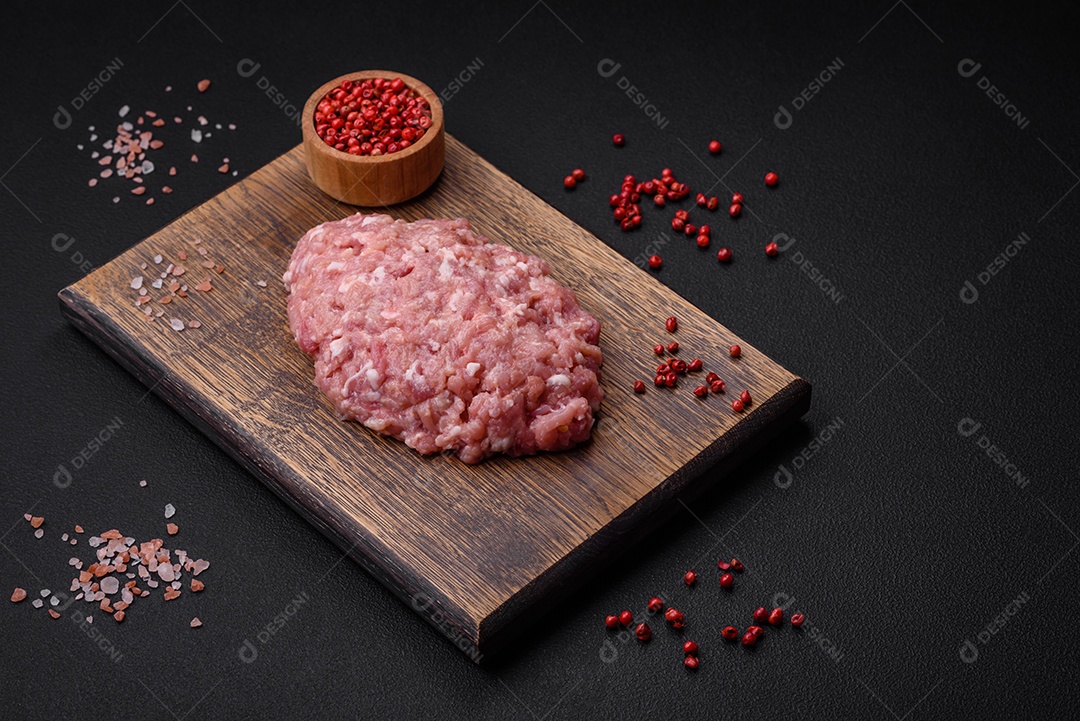 Almôndegas cruas de carne picada, carne de porco ou frango com sal, especiarias e ervas sobre um fundo escuro de concreto