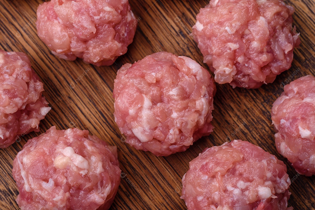 Almôndegas cruas de carne picada, carne de porco ou frango com sal, especiarias e ervas sobre um fundo escuro de concreto