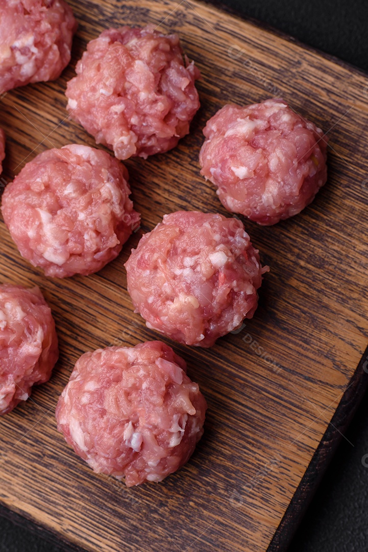 Almôndegas cruas de carne picada, carne de porco ou frango com sal, especiarias e ervas sobre um fundo escuro de concreto