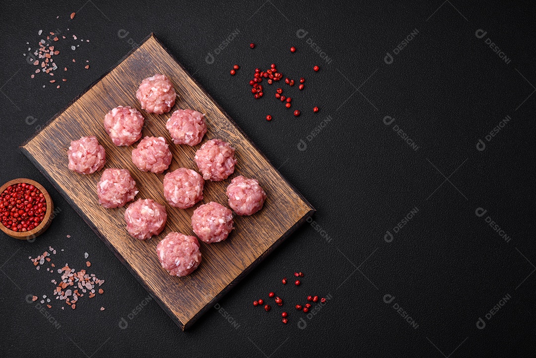 Almôndegas cruas de carne picada, carne de porco ou frango com sal, especiarias e ervas sobre um fundo escuro de concreto