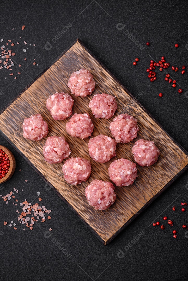 Almôndegas cruas de carne picada, carne de porco ou frango com sal, especiarias e ervas sobre um fundo escuro de concreto