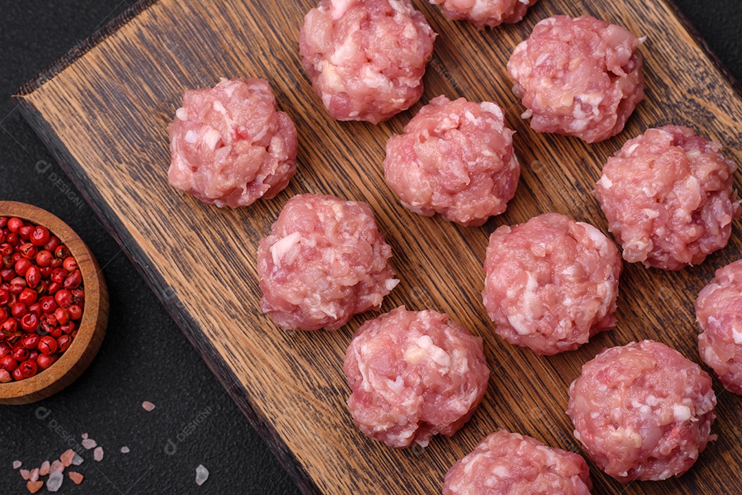 Almôndegas cruas de carne picada, carne de porco ou frango com sal, especiarias e ervas sobre um fundo escuro de concreto
