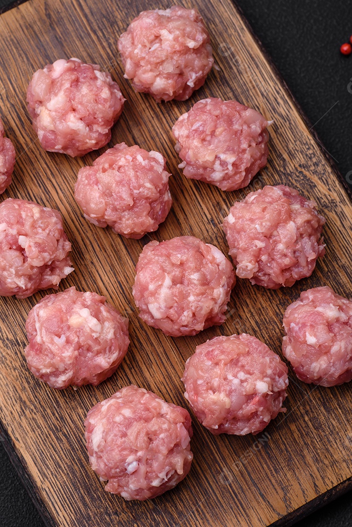 Almôndegas cruas de carne picada, carne de porco ou frango com sal, especiarias e ervas sobre um fundo escuro de concreto