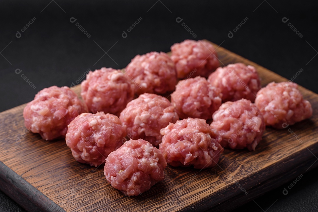 Almôndegas cruas de carne picada, carne de porco ou frango com sal, especiarias e ervas sobre um fundo escuro de concreto