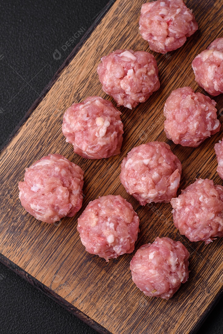 Almôndegas cruas de carne picada, carne de porco ou frango com sal, especiarias e ervas sobre um fundo escuro de concreto