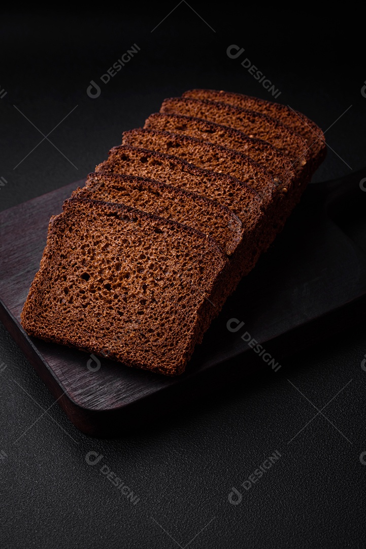 Delicioso pão integral fresco com grãos e sementes cortados em uma tábua de madeira sobre um fundo escuro de concreto