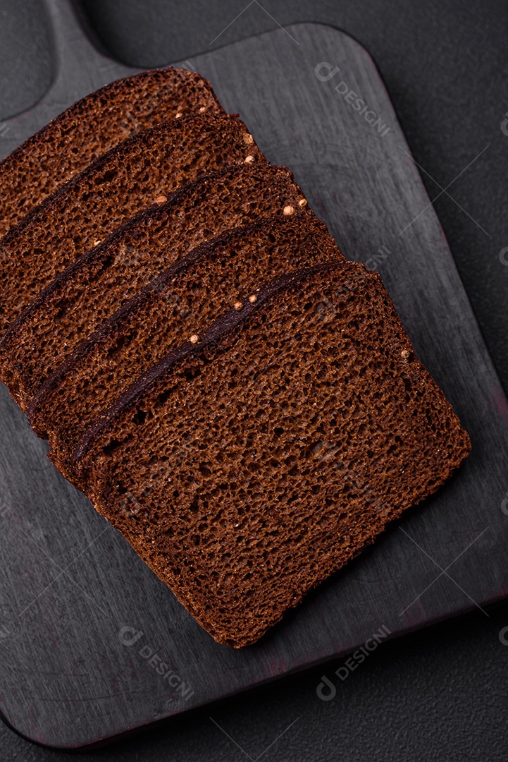 Delicioso pão integral fresco com grãos e sementes cortados em uma tábua de madeira sobre um fundo escuro de concreto