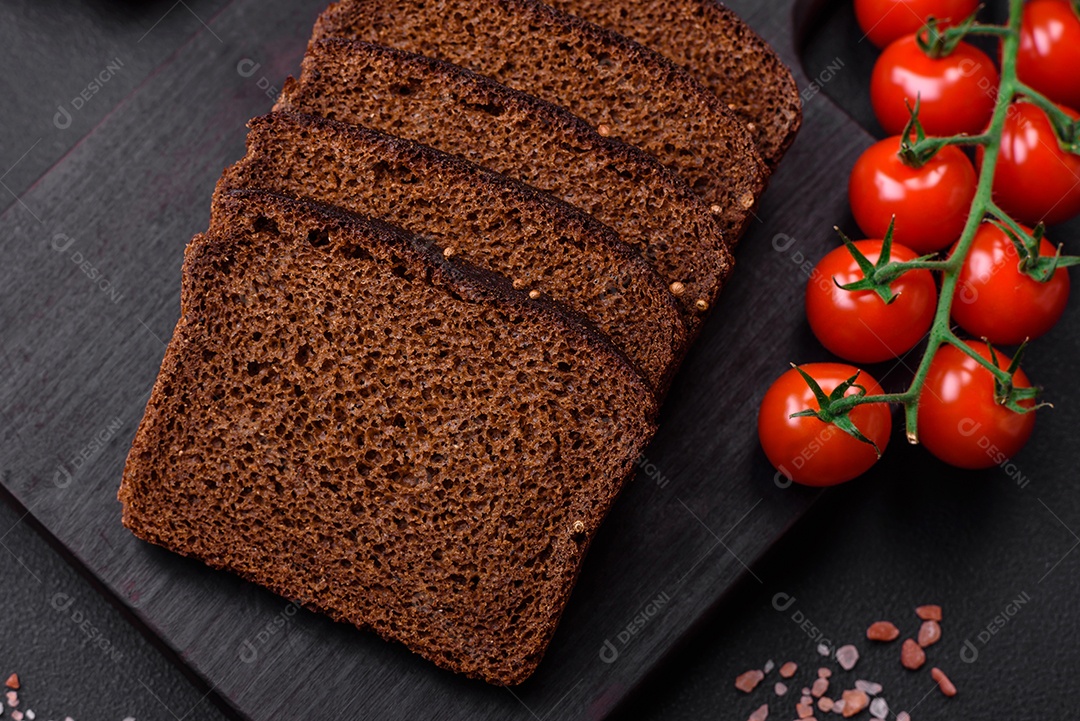Delicioso pão integral fresco com grãos e sementes cortados em uma tábua de madeira sobre um fundo escuro de concreto
