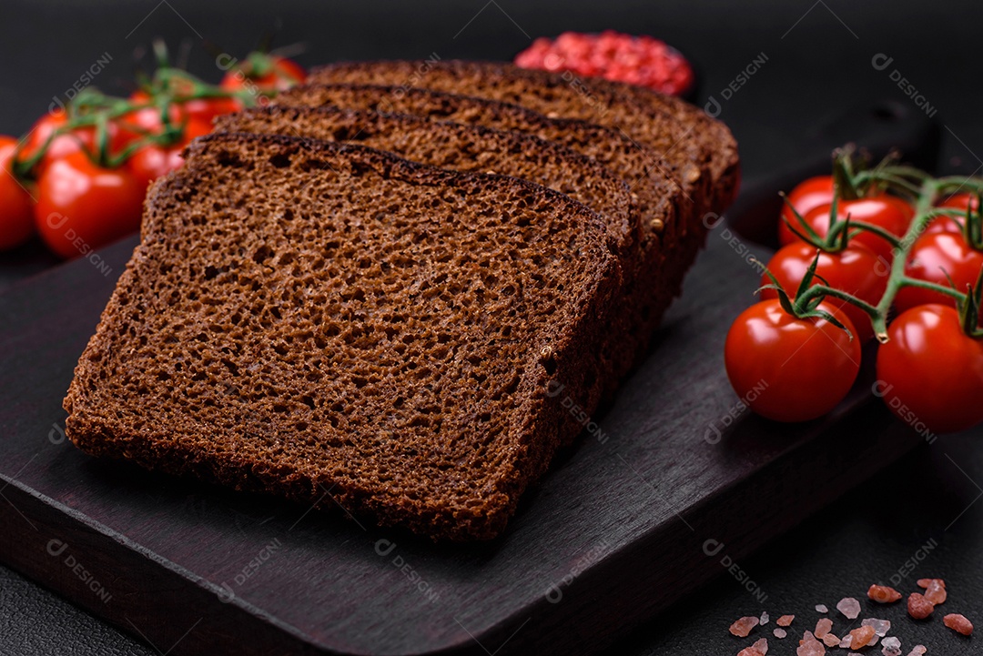 Delicioso pão integral fresco com grãos e sementes cortados em uma tábua de madeira sobre um fundo escuro de concreto