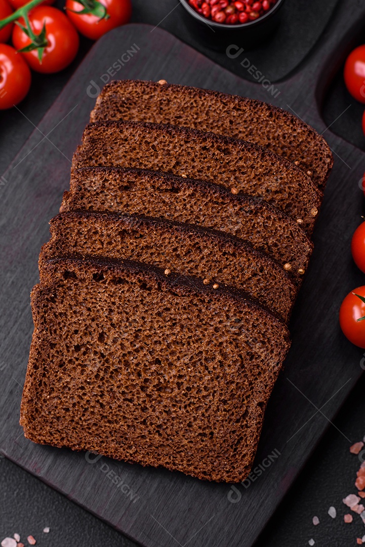 Delicioso pão integral fresco com grãos e sementes cortados em uma tábua de madeira sobre um fundo escuro de concreto