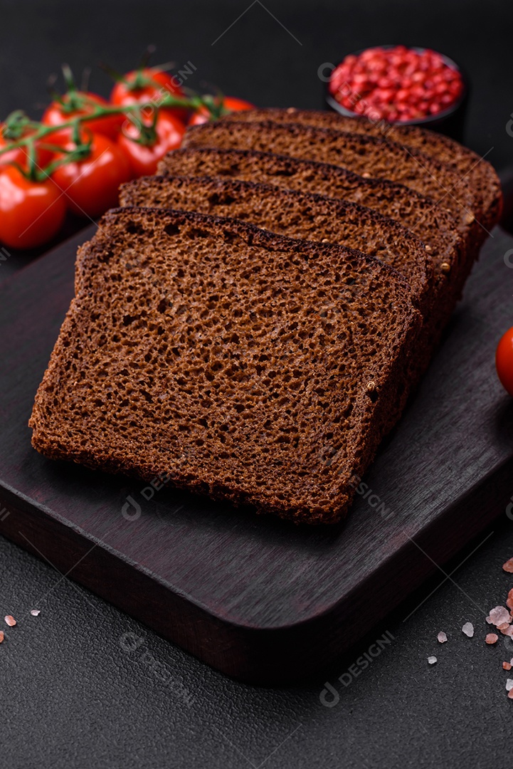 Delicioso pão integral fresco com grãos e sementes cortados em uma tábua de madeira sobre um fundo escuro de concreto