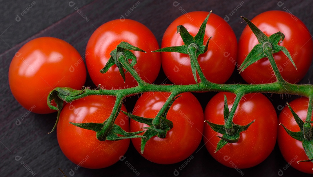 Deliciosos tomates cereja frescos em um galho com especiarias e ervas sobre um fundo escuro de concreto