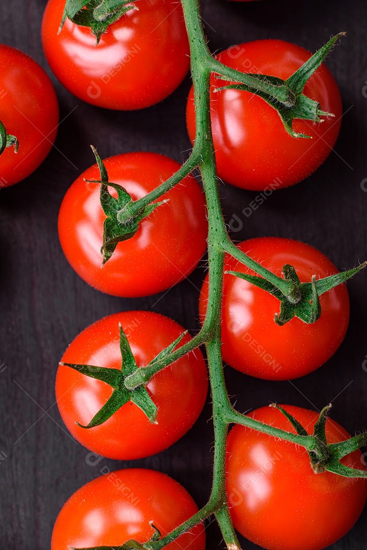 Deliciosos tomates cereja frescos em um galho com especiarias e ervas sobre um fundo escuro de concreto