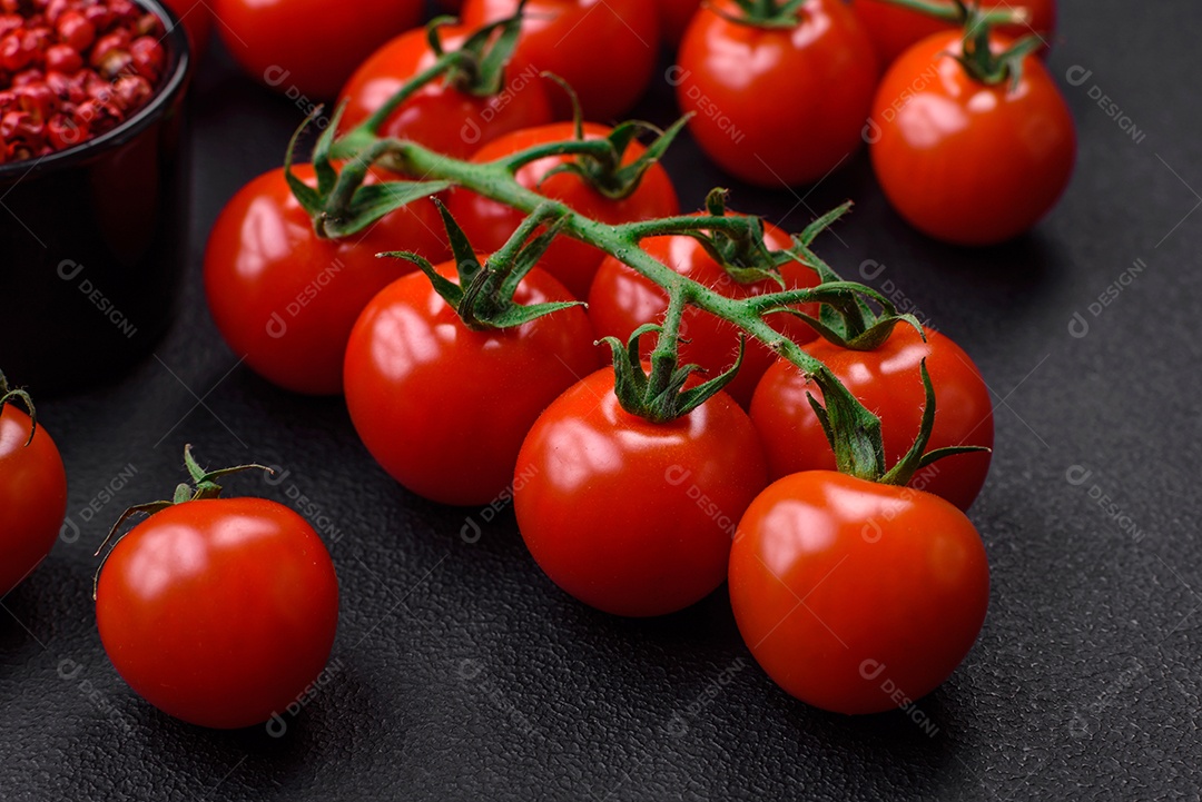 Deliciosos tomates cereja frescos em um galho com especiarias e ervas sobre um fundo escuro de concreto