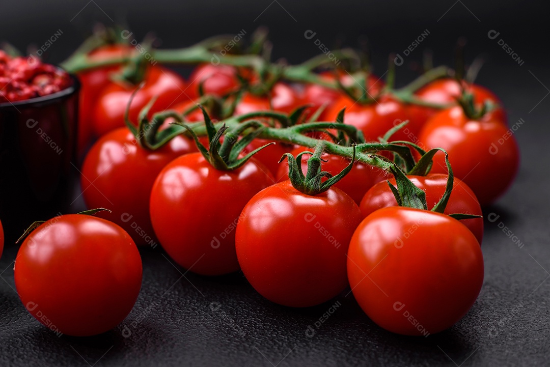 Deliciosos tomates cereja frescos em um galho com especiarias e ervas sobre um fundo escuro de concreto