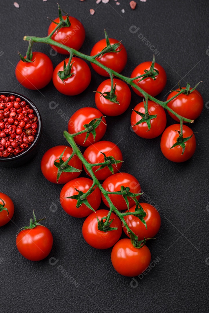 Deliciosos tomates cereja frescos em um galho com especiarias e ervas sobre um fundo escuro de concreto