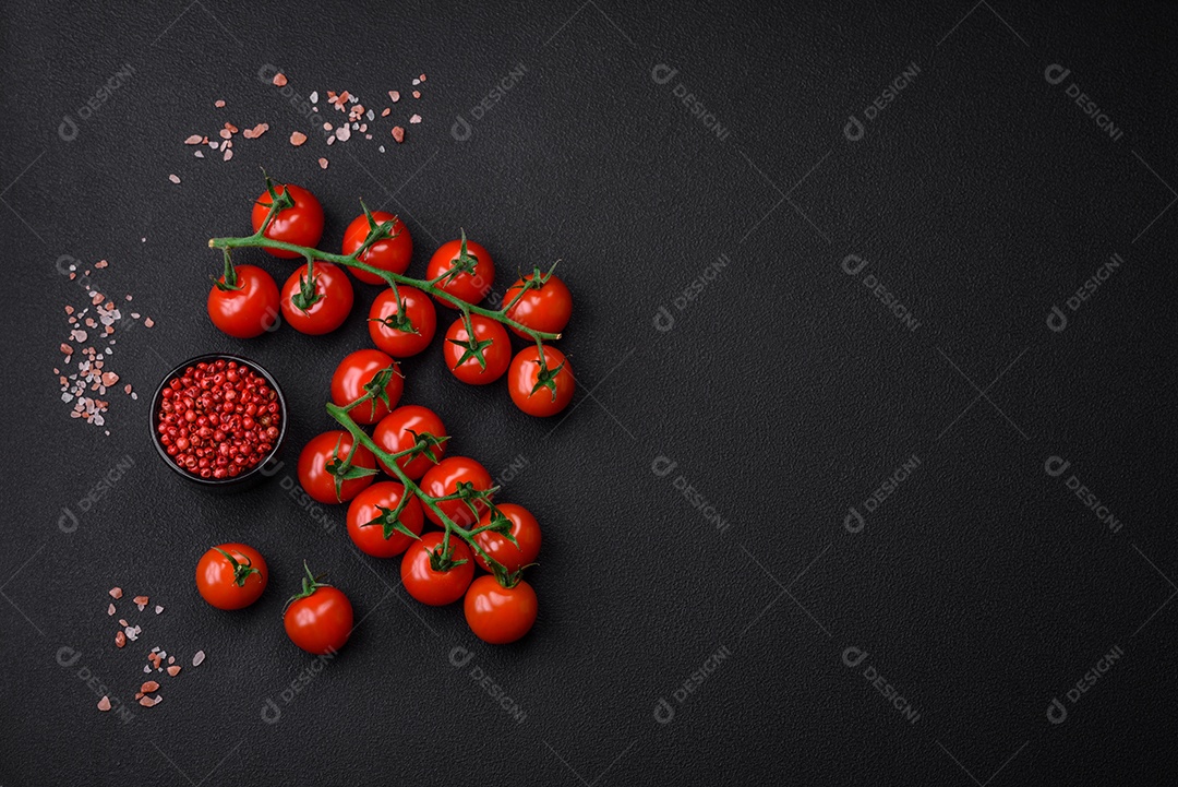 Deliciosos tomates cereja frescos em um galho com especiarias e ervas sobre um fundo escuro de concreto