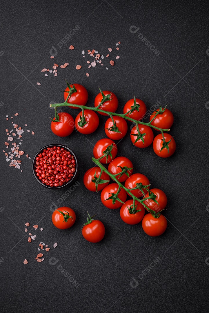 Deliciosos tomates cereja frescos em um galho com especiarias e ervas sobre um fundo escuro de concreto