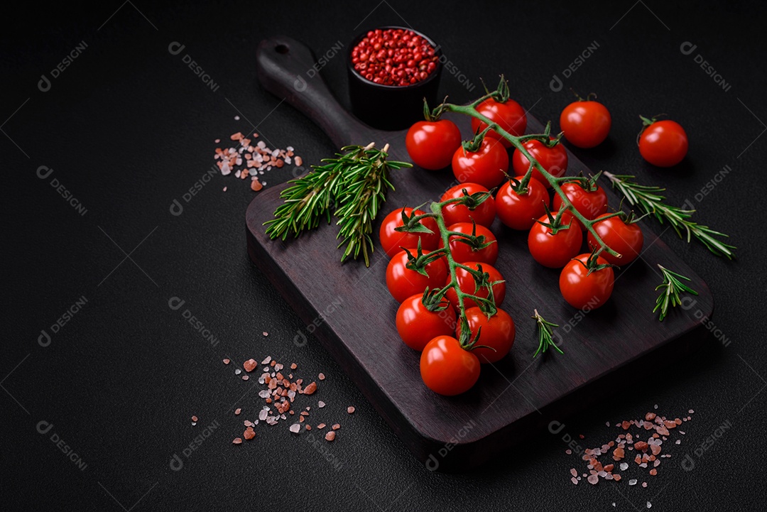 Deliciosos tomates cereja frescos em um galho com especiarias e ervas sobre um fundo escuro de concreto