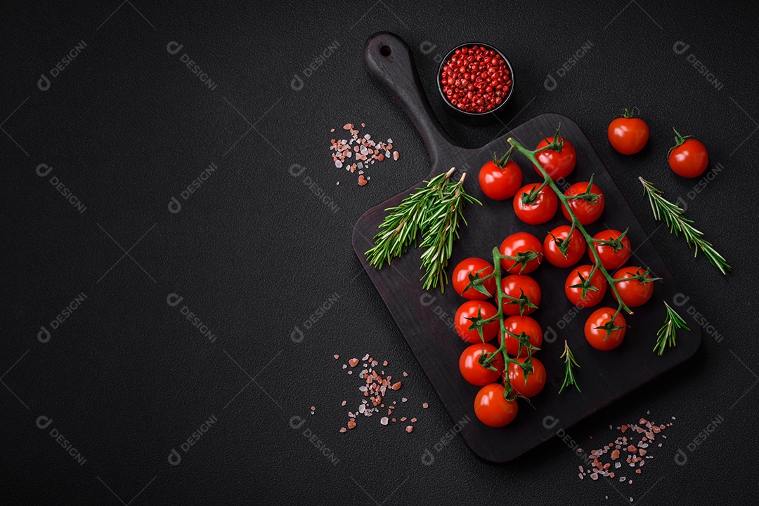 Deliciosos tomates cereja frescos em um galho com especiarias e ervas sobre um fundo escuro de concreto